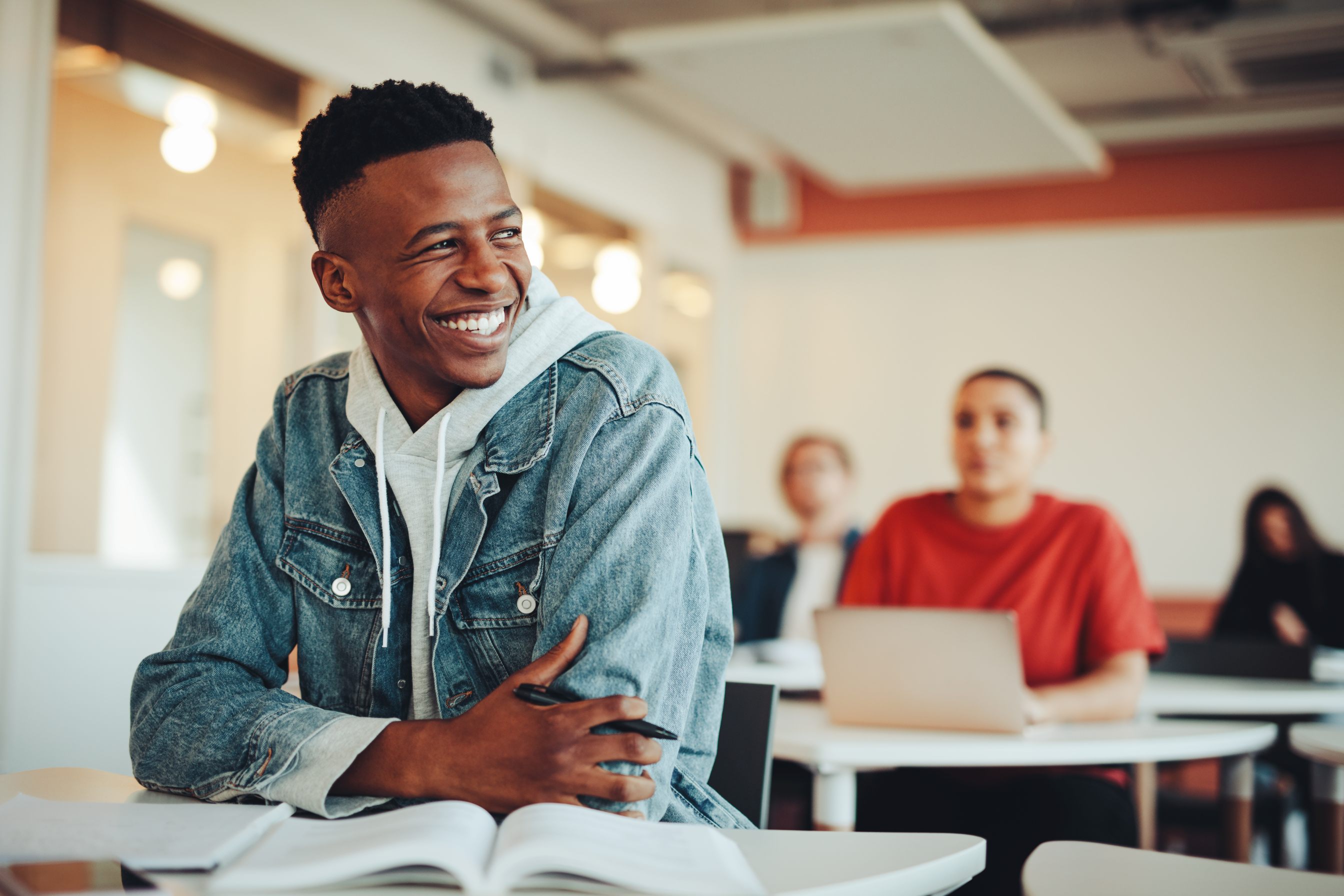 Ein lächelnder junger Mann sitzt im Klassenzimmer und genießt sein Studium