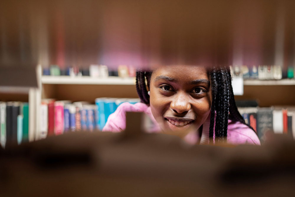 Studentin in der Bibliothek, lächelt beim Lernen für Master-Stipendien und verfolgt ihre Träume.