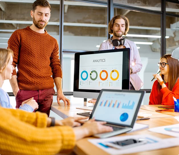 Besprechungsteam analysiert Marketing‑Analytics‑Dashboard auf Computerbildschirmen im Büro.