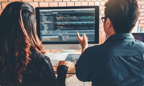 Entwickler besprechen HTML5‑Code, der in einer Lernumgebung auf einem Monitor angezeigt wird.