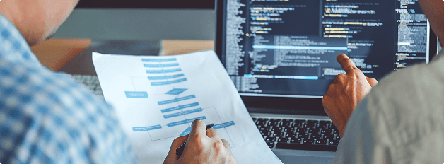 Two developers collaborating on a project, reviewing a flowchart and coding in JavaScript and JSON on a laptop. Understanding how JavaScript and JSON are used in Django is key for efficient web development.