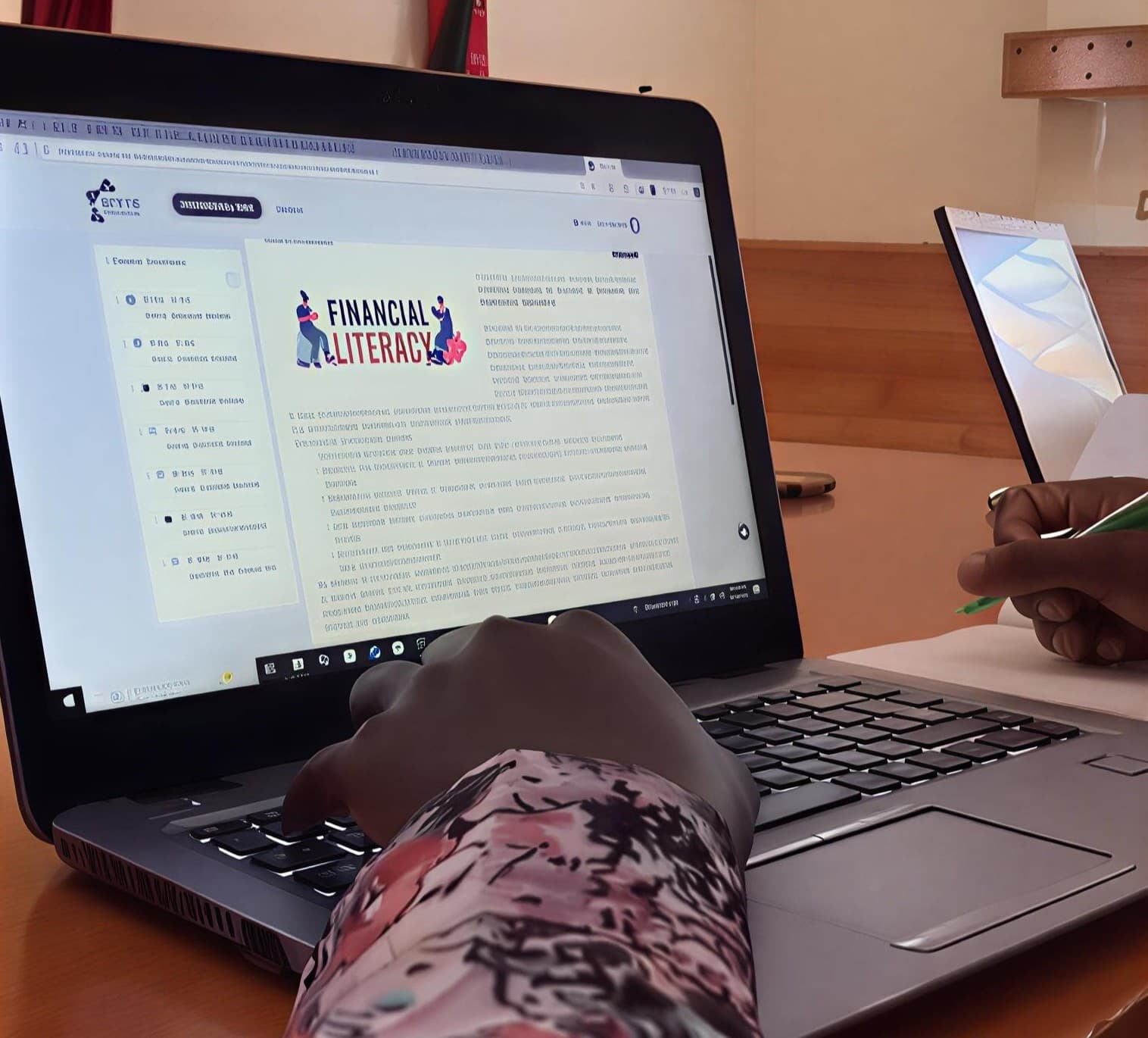 A person using a laptop to take an online financial literacy course, with the WEZESHA logo visible in the corner of the screen.