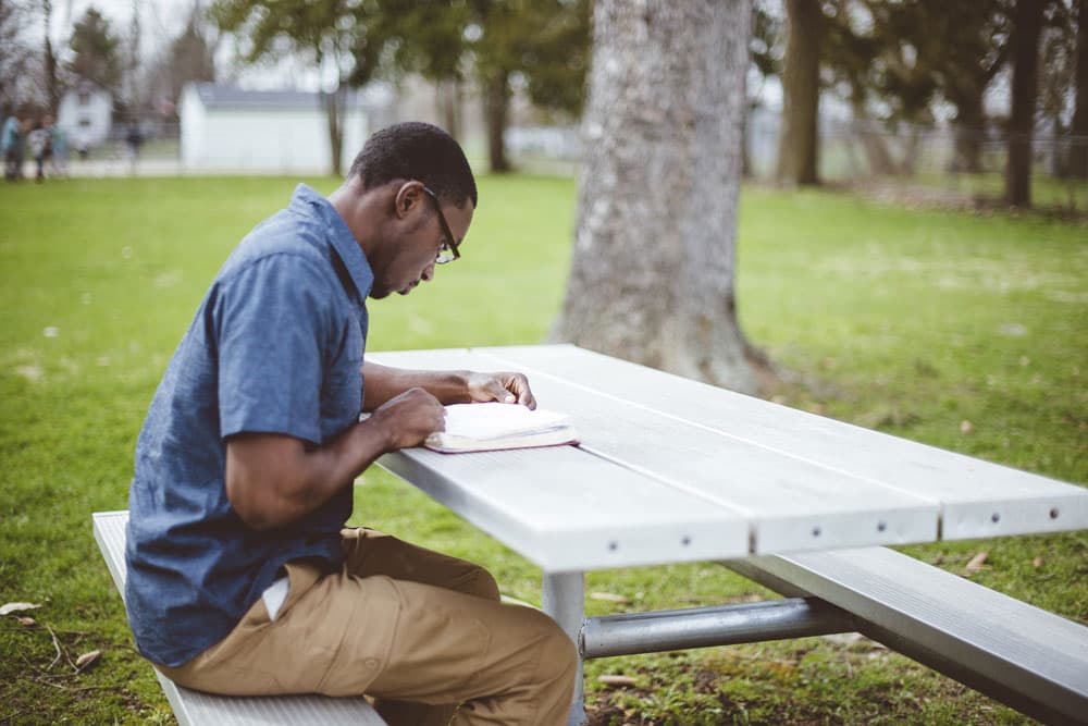 Student studying outdoors, preparing for a second degree scholarship while reading a book.