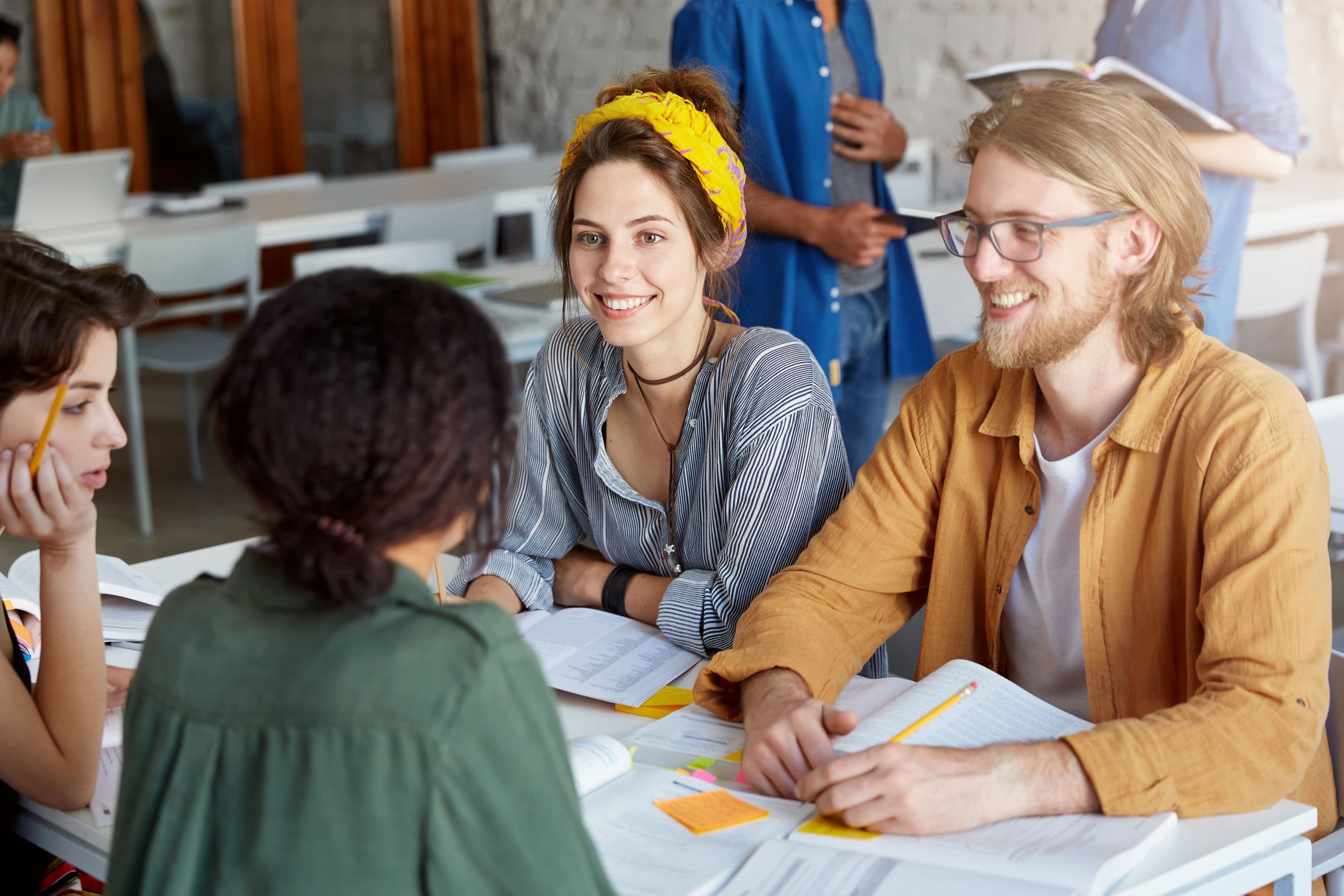 Group of young adults sitting at a table and discussing, smiling and collaborating in a classroom setting.