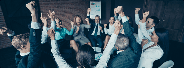 Team feiert gemeinsam mit erhobenen Armen bei einer Besprechung im modernen Büro.